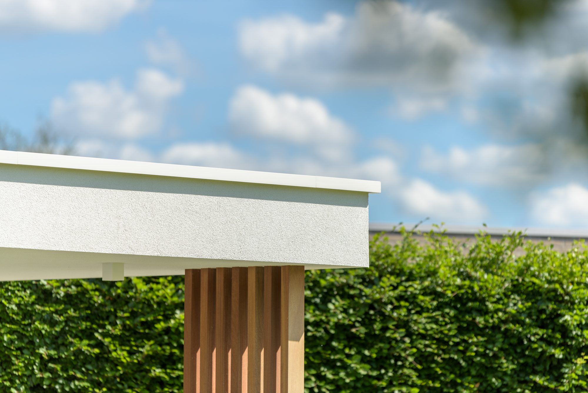 Dakrand van moderne poolhouse met witte crepi, aluminium profiel en iroko sierpalen
